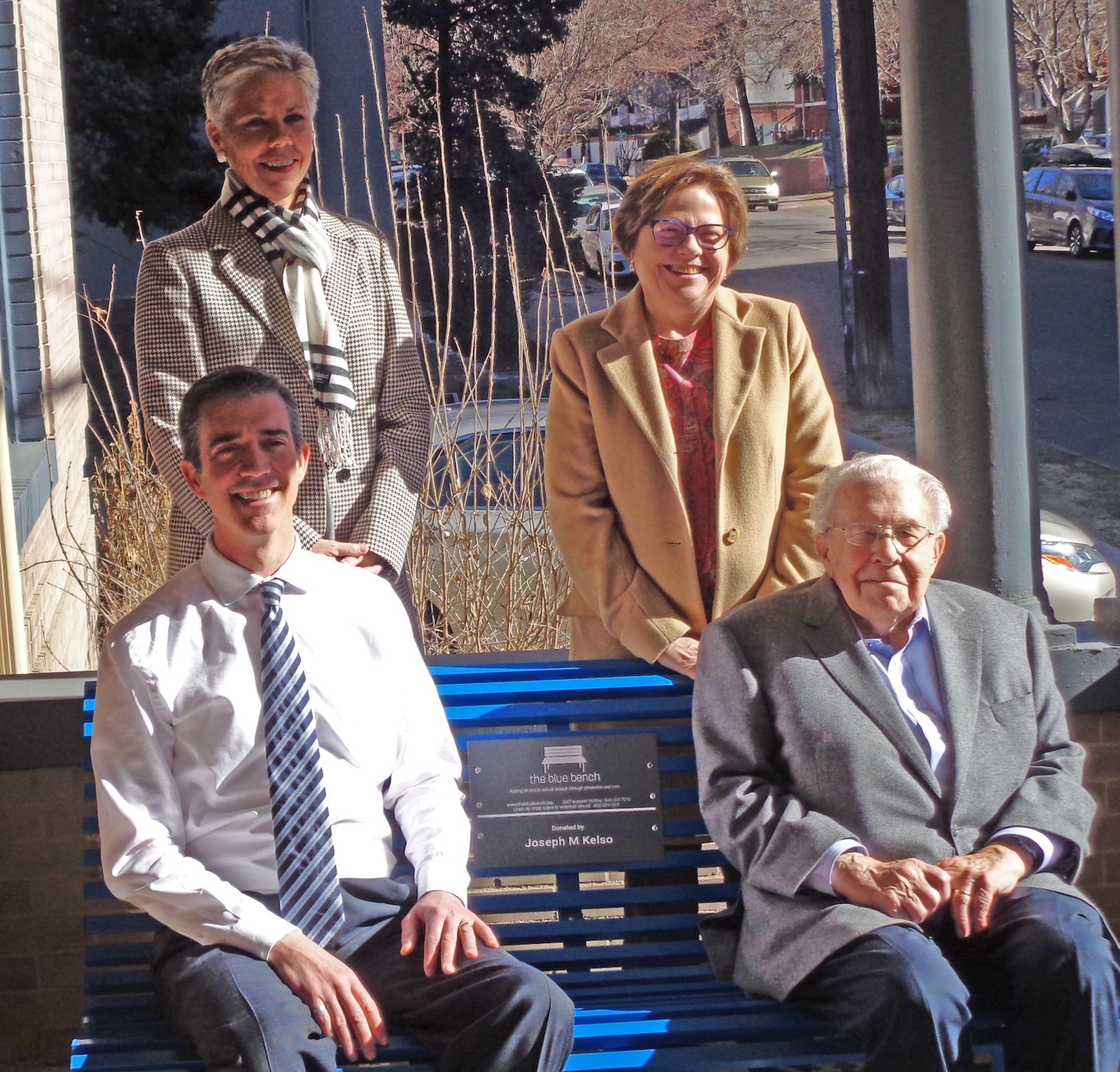 Photo of leadership members from TheBlueBench organization sitting or standing near a blue bench.