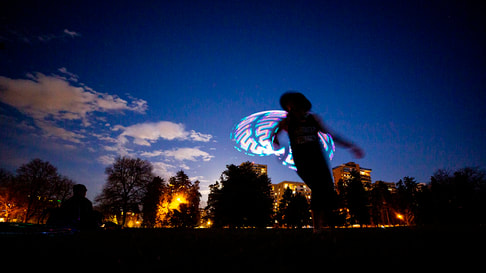 Photo at dusk of Heather Farley whips a hula hoop around her body in Cheesman park